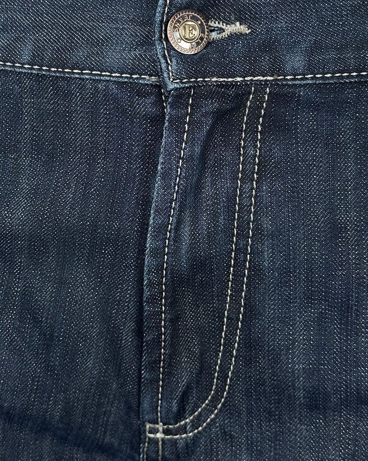 Detaljan prikaz regular fit farmerica za visoke, produžena nogavica, tamni teksas sa belim štepovima. Detaljan prikaz regular fit farmerica za visoke, produžena nogavica, tamni teksas sa belim štepovima.