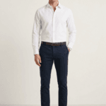 Muškarac nosi elegantnu belu blago strukiranu košulju marke ELIT u kombinaciji sa crnim pantalonama i braon kaišem. elegantna bela muška košulja.