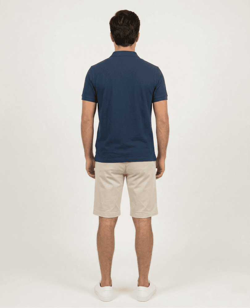 Muški bež šorc za svaki dan, opušten stil. Detaljan prikaz bež šorca sa tamno plavom majicom i belim patikama.