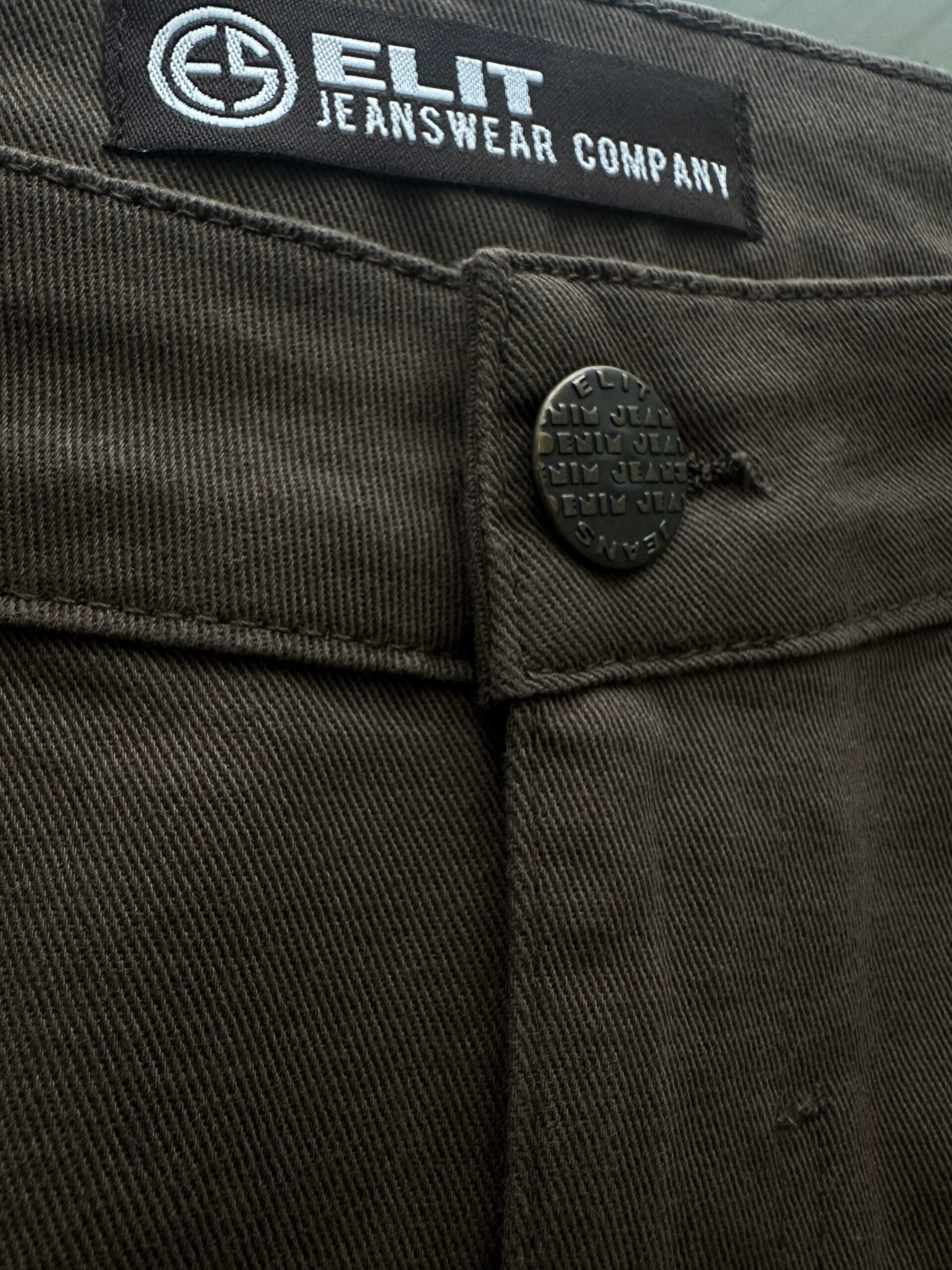 Crna suknja od organskog pamuka - detalj dugmeta Krupni kadar detalja na crnoj suknji od organskog pamuka, sa metalnim dugmetom i ušivenom Elit Jeanswear etiketom.